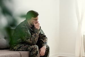 Sad-soldier-in-uniform-covering-his-mouth-while-sitting-on-a-sofa-1019966974_1258x838