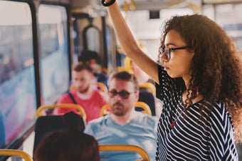 Serious-young-curly-girl-standing-in-a-bus-full-of-people.-1023588506_1256x838